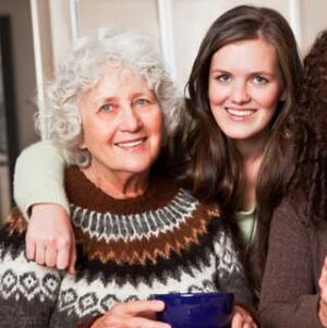 Both an older and younger woman. The younger woman has her arm around the older woman, and the older woman is wearing a decorative yoke sweater.