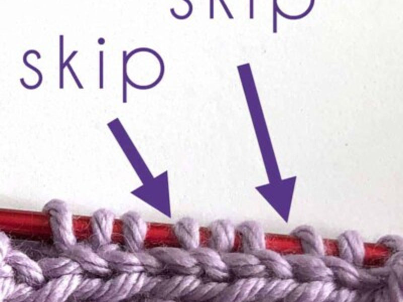 Stitches picked up along a knitted edge, with arrows marking the skipped spots