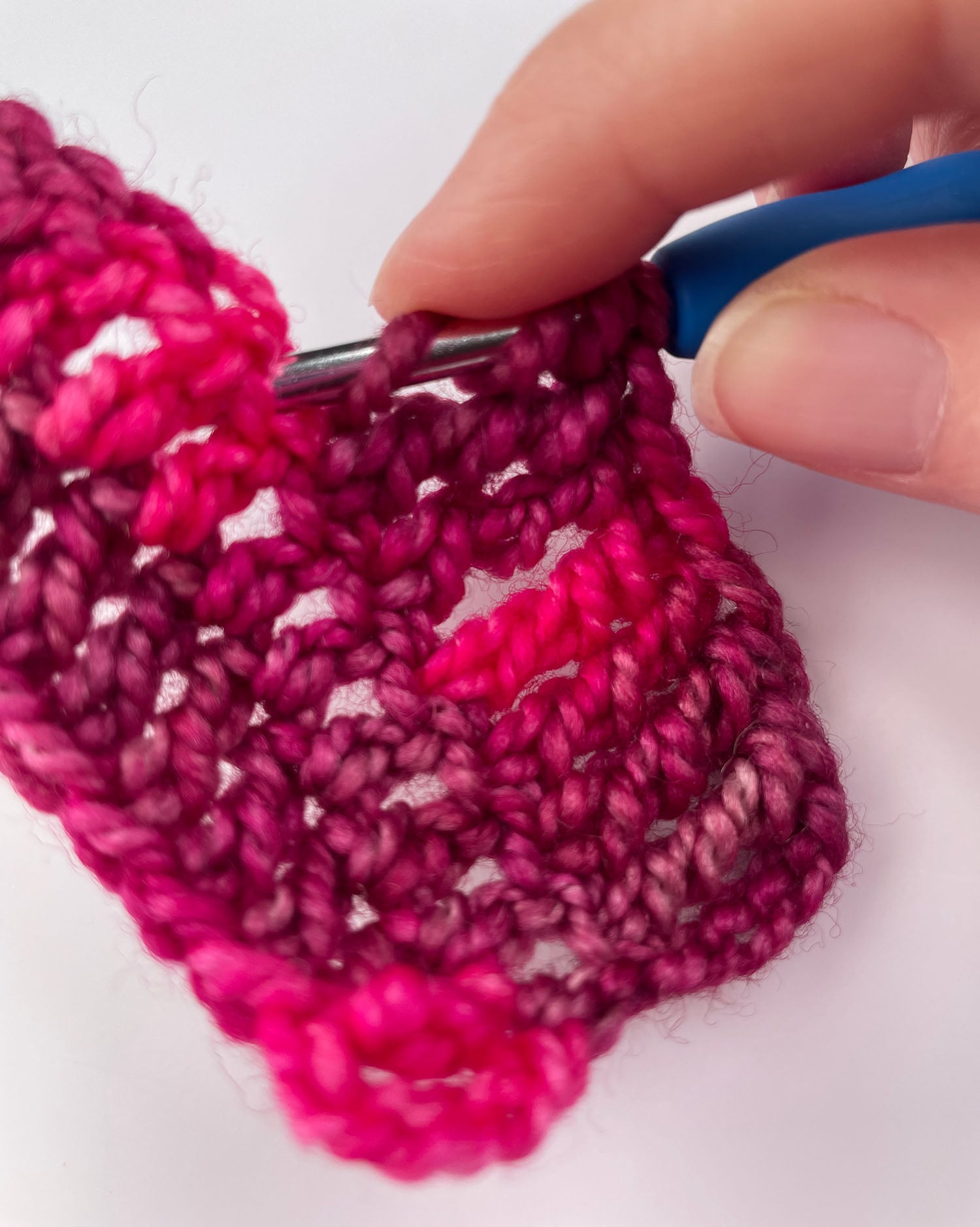 Fingers holding three yarn overs in place on the hook while it is inserted into the stitch.