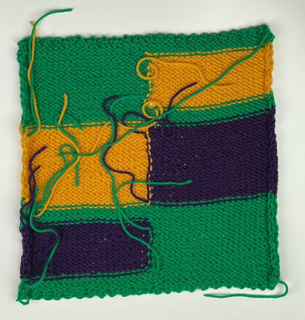 Wrong side of the Crop Rotation intarsia knit square before weaving in, with loose yarn ends at each color join