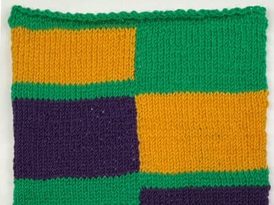 Crop Rotation knit intarsia square in Christmas Green, Italian Plum, and Golden Yellow, with color blocks that trade sides between green bands