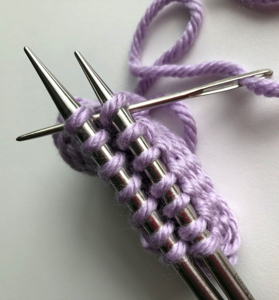 Darning needle inserted knitwise through the first stitch on both needles for the Finchley Graft