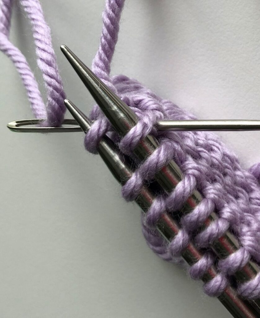 Darning needle inserted purlwise through the first stitch on both needles for the Finchley Graft
